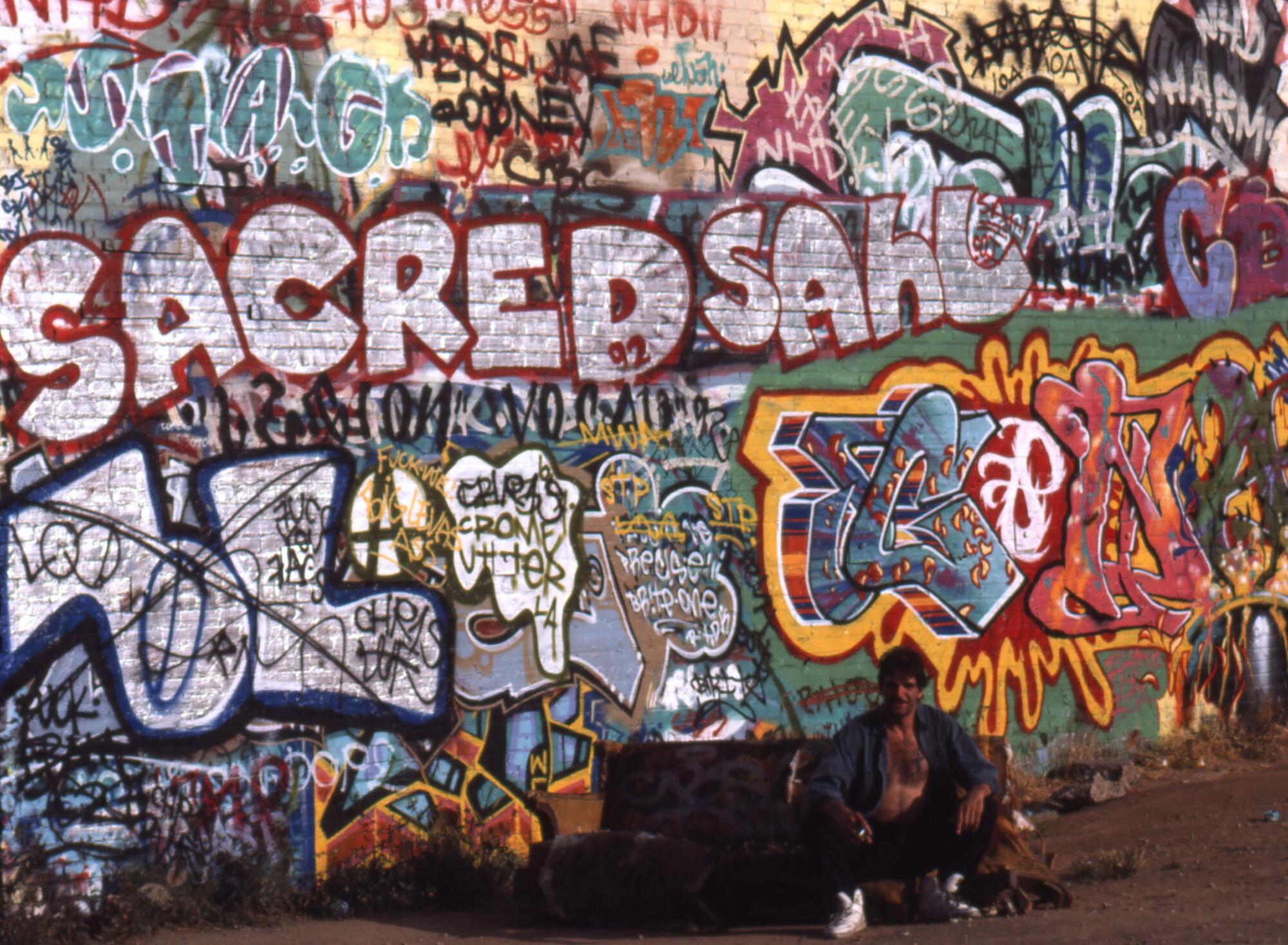 A man in front of a wall covered with graffiti.