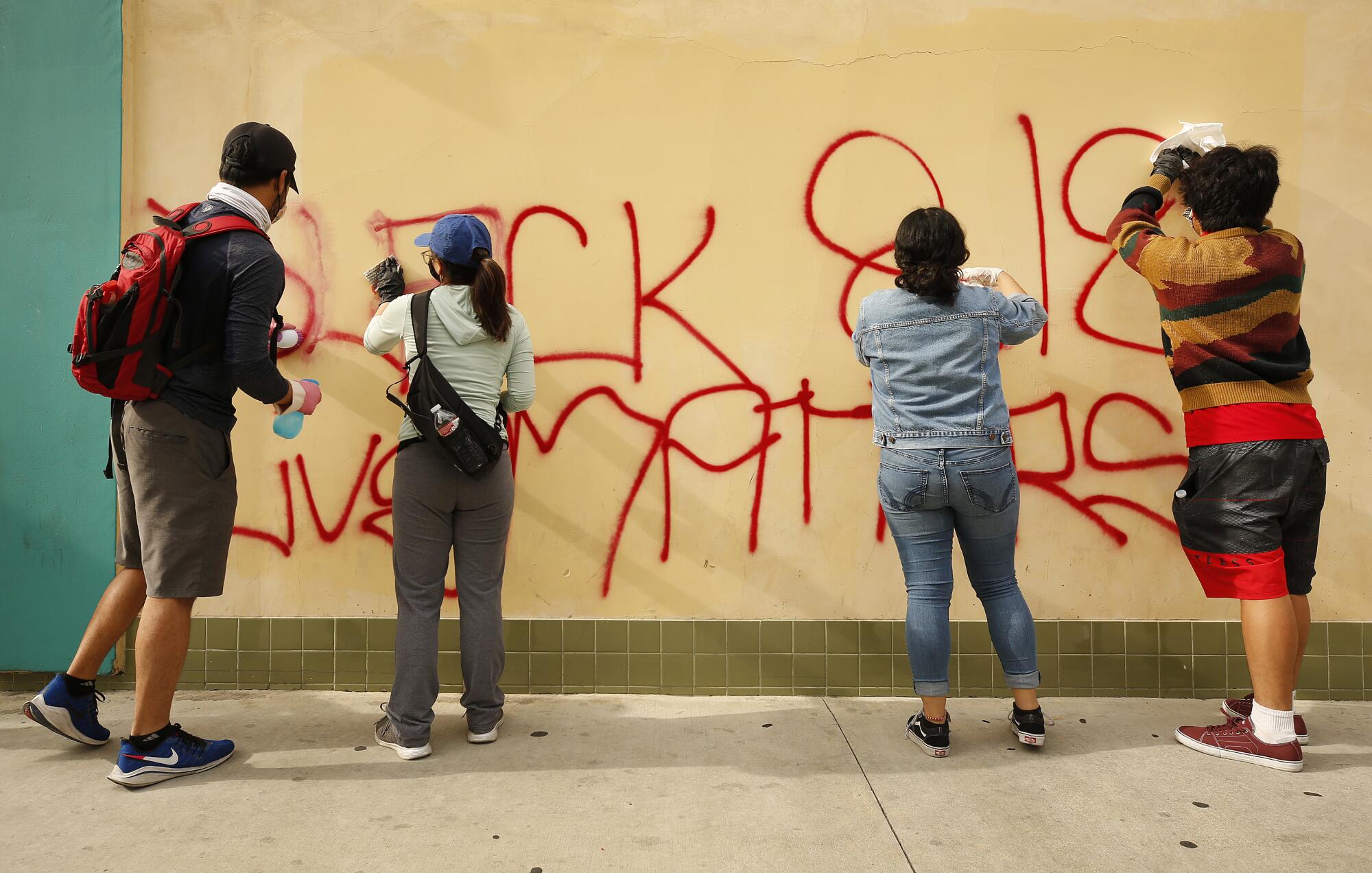 Four people scrub graffiti on a wall.