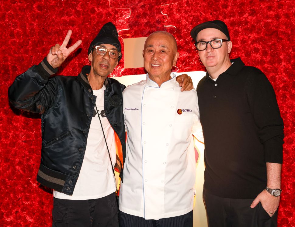 Three men stand arm in arm in front of a red background