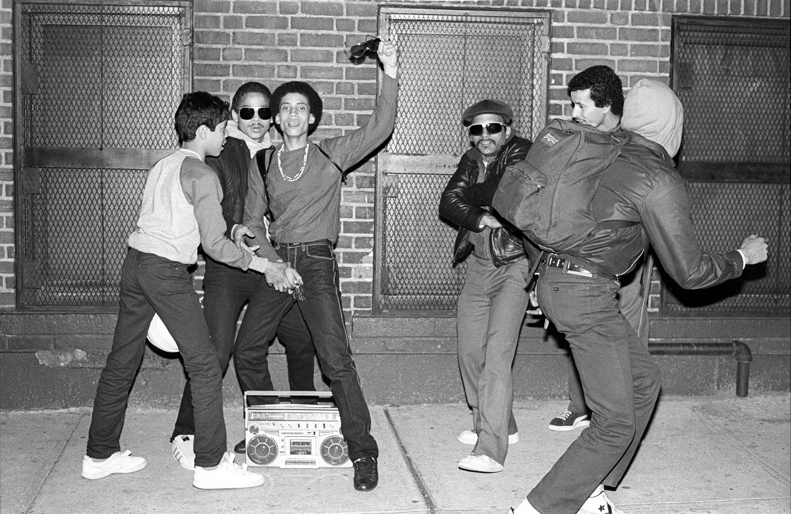 Men hanging out on a sidewalk with a boombox.