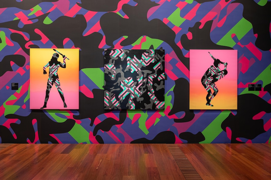 A wall in a gallery with bright splashes of pink, green and blue, with outline portraits of Aboriginal warriors on top