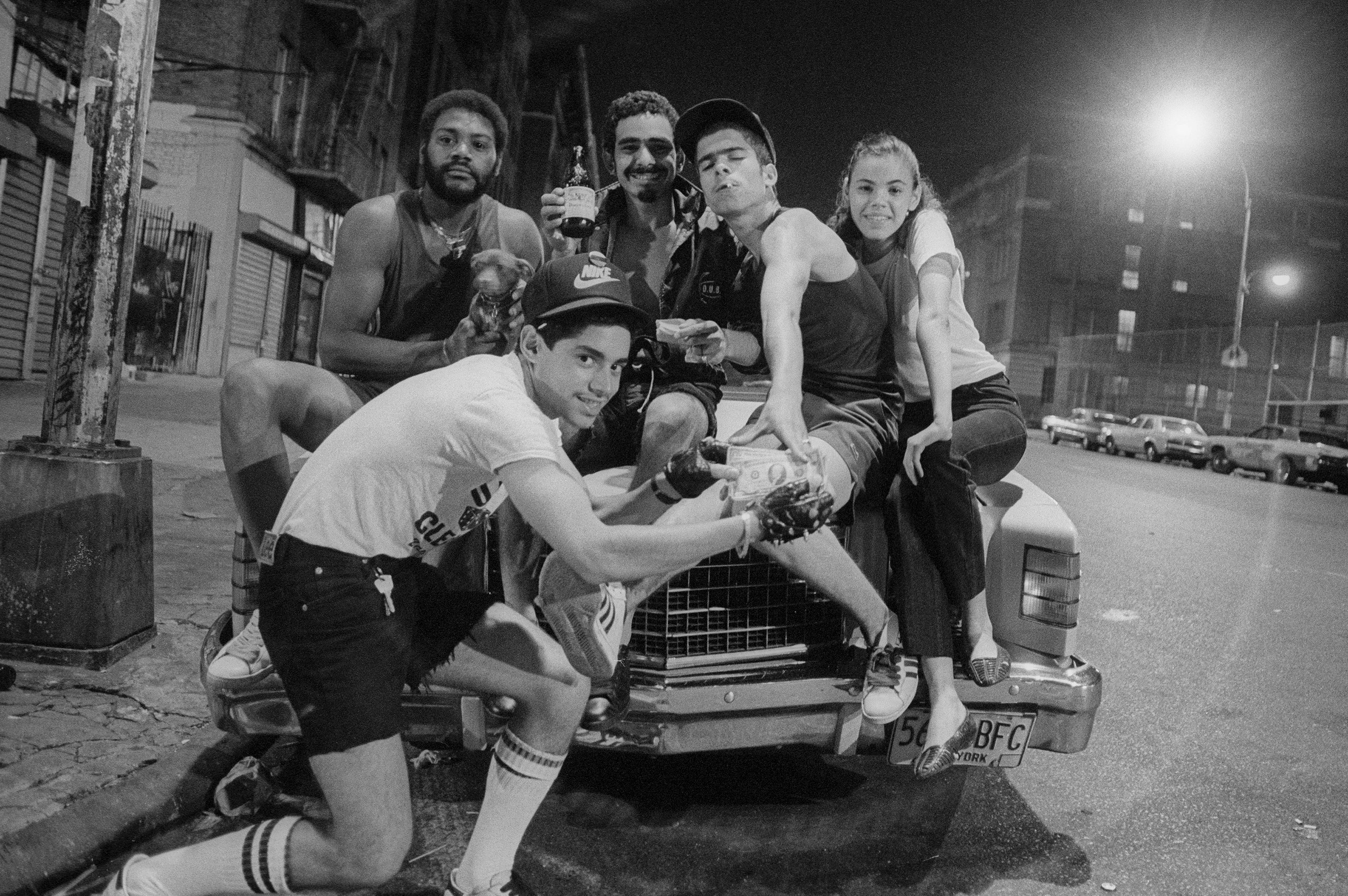 A group of youth posing for a photo sitting on the hood of a car.