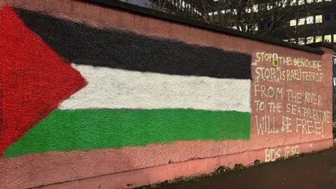 BBC A wall at the royal victoria hospial in belfast  which has been daubed with the phrase “from the river to the sea, Palestine will be free”.  a Palestinian flag has also been painted on the wall