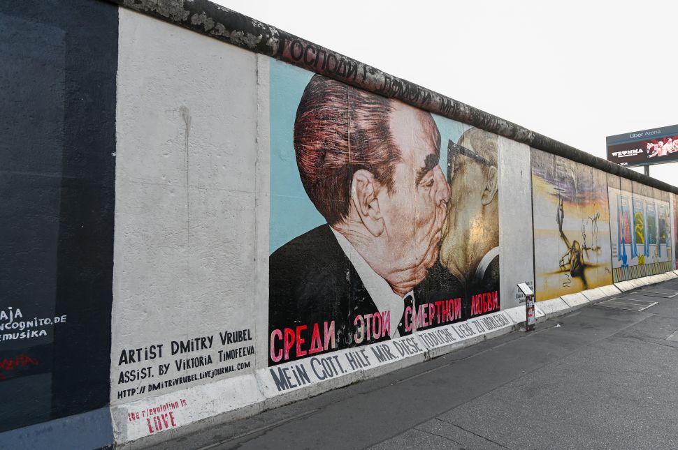 A mural on the Berlin Wall at the East Side Gallery shows Soviet leader Leonid Brezhnev and East German leader Erich Honecker in a famous embrace, surrounded by painted text and graffiti on the lower wall.