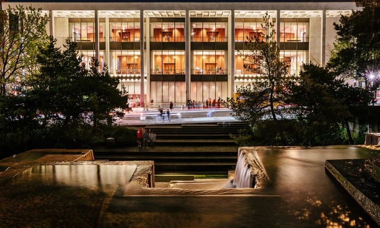 exterior of the Keller Auditorium at night showing a wide building lit from within, viewed from the Keller Fountain, whose geometric lines mirror the auditorium's architecture