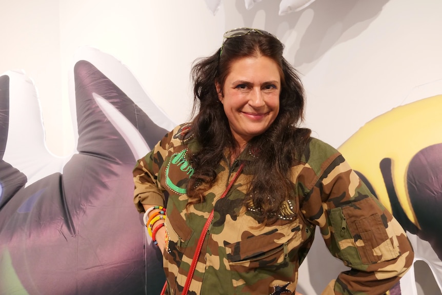 A woman wearing camouflage-style clothing standing in front of a painted mural