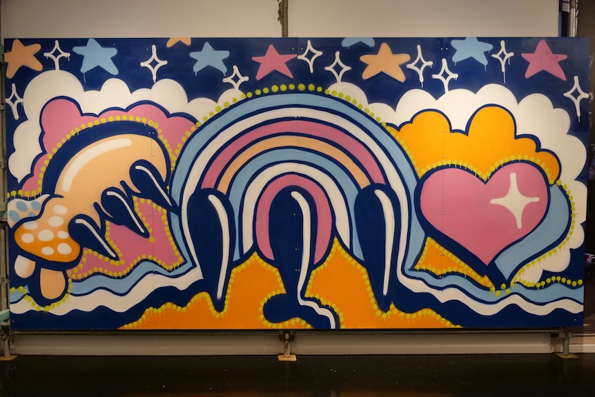 A vibrant bubble graffiti mural featuring hearts, claws, clouds, and rainbows, painted in dazzling blues, oranges and pinks