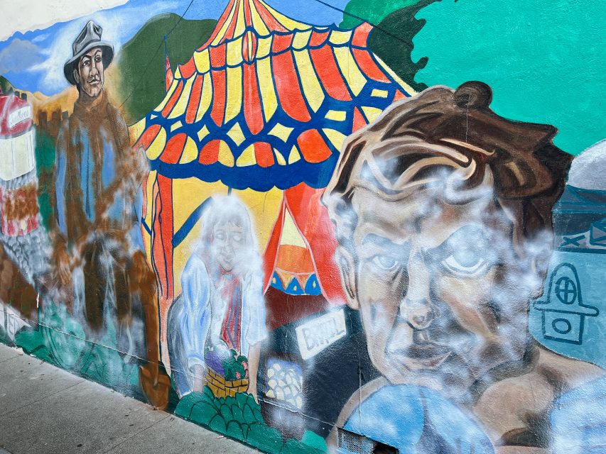 Colorful mural featuring figures, a tent-like structure, and various scenes blending into each other on a wall.