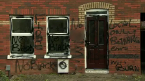 BBC The front of a house covered in graffiti. The graffiti reads 