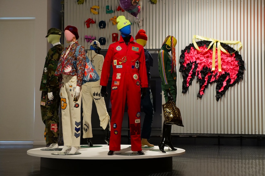 Colourful mannequins stand on a circular platform in an art exhibit, wearing streetwear designed by a graffiti artist