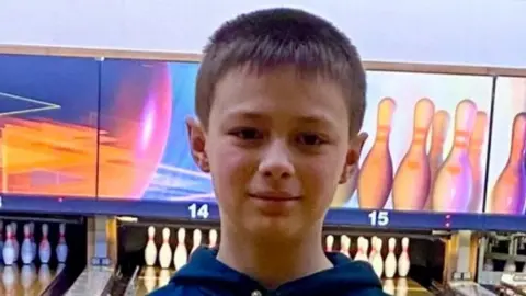 West Midlands Police Leo looking straight at the camera. Ten-pin bowling is behind him with an alley leading to a set of pins.