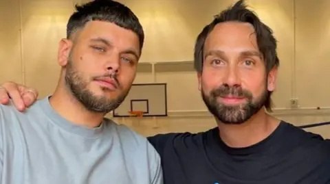 James Bennett Two bearded men side by side. One wearing a grey t-shirt, one wearing a black t-shirt