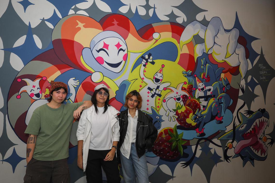 ST20250217_202575600248/dlstreetart/Taryn Ng/Dillon Loh//   (from left) Soup, Jade and Zeefish are among young artists part of Scape's Street Art Residency programme. The 24-year-olds are pictured with their mural which they completed collectively at Scape on Feb 17, 2025. ST PHOTO: TARYN NG