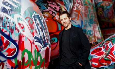 Glenn Martens at the end of the Diesel show in Milan: he stands in front of the graffiti-covered backdrop wearing a black top and jacket.