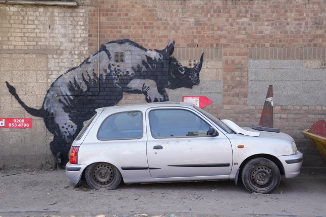 A new artwork unveiled by Banksy, depicting a rhinoceros which looks as though it is climbing on top of a car, the eighth artwork in his animal-themed collection, on Westmoor Street in Charlton, south east London. Picture date: Monday August 12, 2024. PA Photo. See PA story ARTS Banksy. Photo credit should read: Lucy North/PA Wire