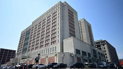 Getty Images A woman using a mobile phone walks past the Metropolitan Detention Center in Brooklyn, New York.