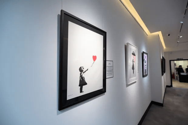 Gallery wall with framed artwork, including a prominent piece depicting a girl releasing a red heart-shaped balloon.