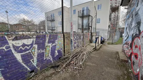 BBC A low brick wall with graffiti all over it and a building behind it.