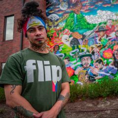 Talilo Marfil, wearing the flag of the Philippines as bandana and a shirt with the word, 'flip,' (a slang term for Filipino) stands in front of a colorful mural depicting his likeness.