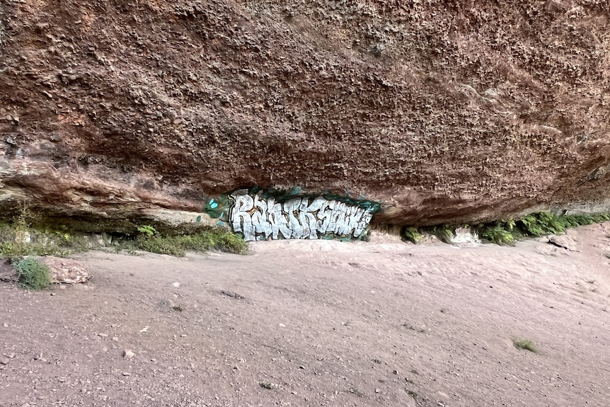 a large rock wall with small spraypainted letters in the distance