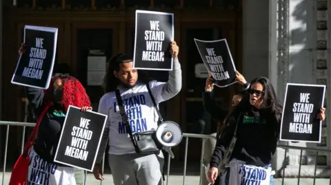 Getty Images Four people stand in a row holding black signs printed with