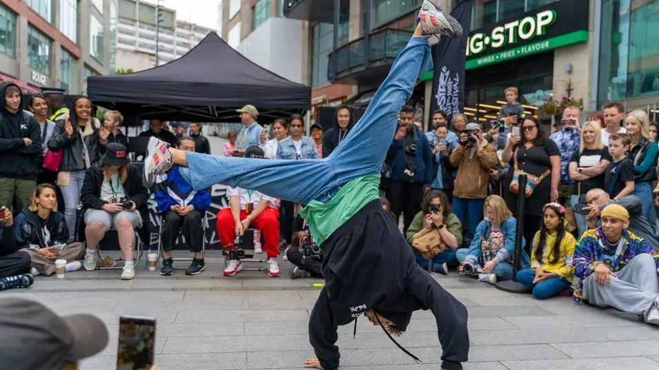 A man performs a handstand in front of crowds in a Birmingham street.