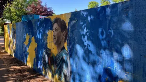 Fiona Callow/BBC A stretch of brick wall spray-painted blue and yellow and featuring the figure of a boy holding a football.