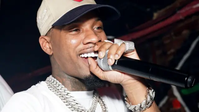 Rapper Tory Lanez hold a microphone for event. E get multiple diamond chains, rings and a silver diamond bracelet.