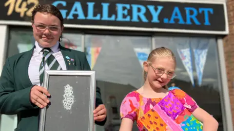 Jon Wright/BBC Two young people stand in front of a shop window. The sign at the top reads