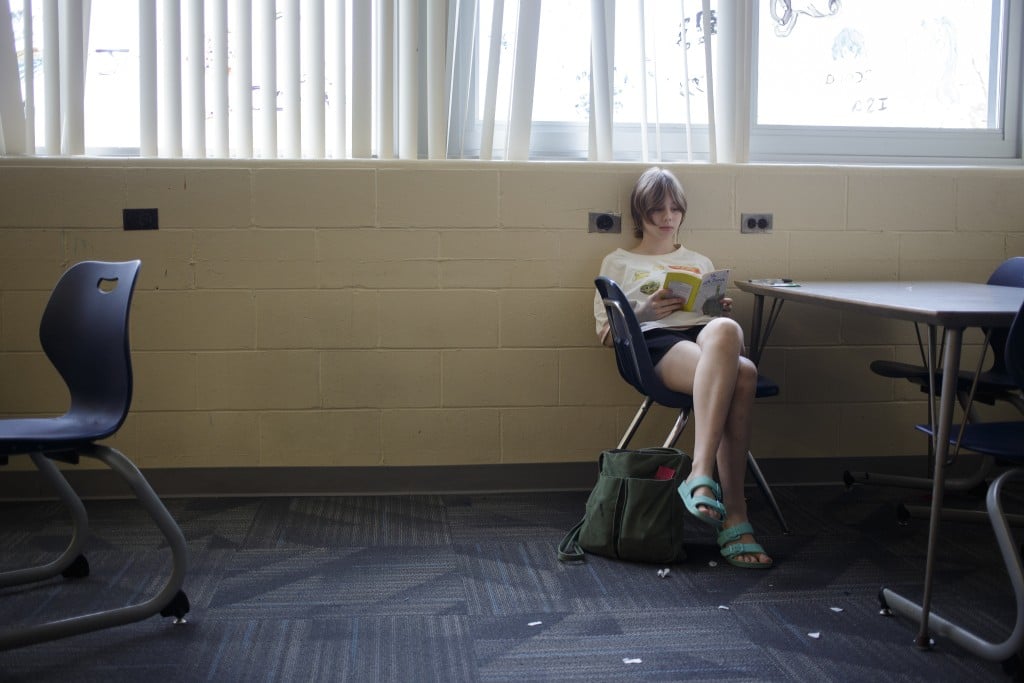 Matti Richards Barnhill sits alone in a classroom, reading a book.