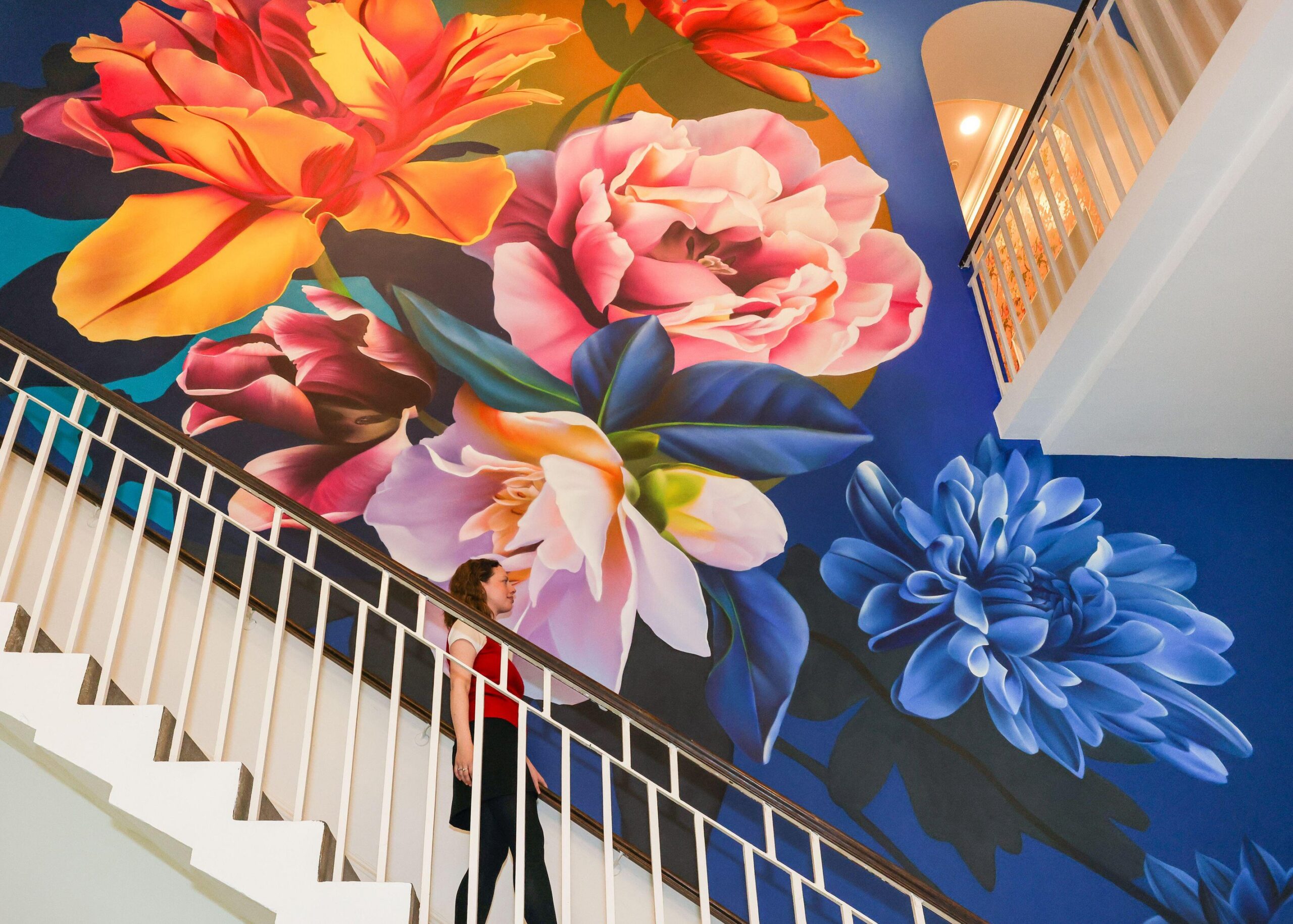 A woman walks up a staircase with a large floral mural in the background.