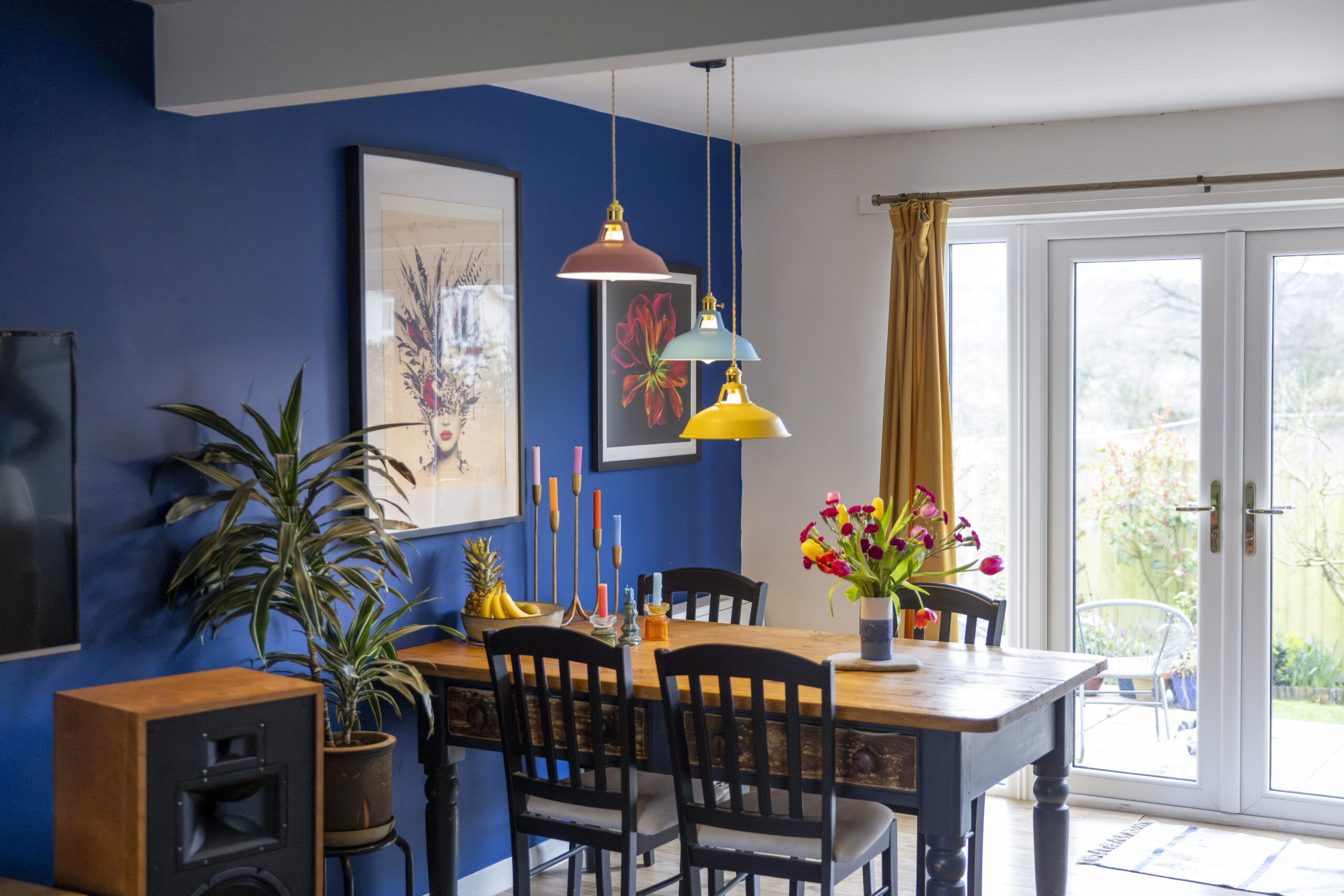 Dining room with blue walls, artwork, and colorful pendant lights.