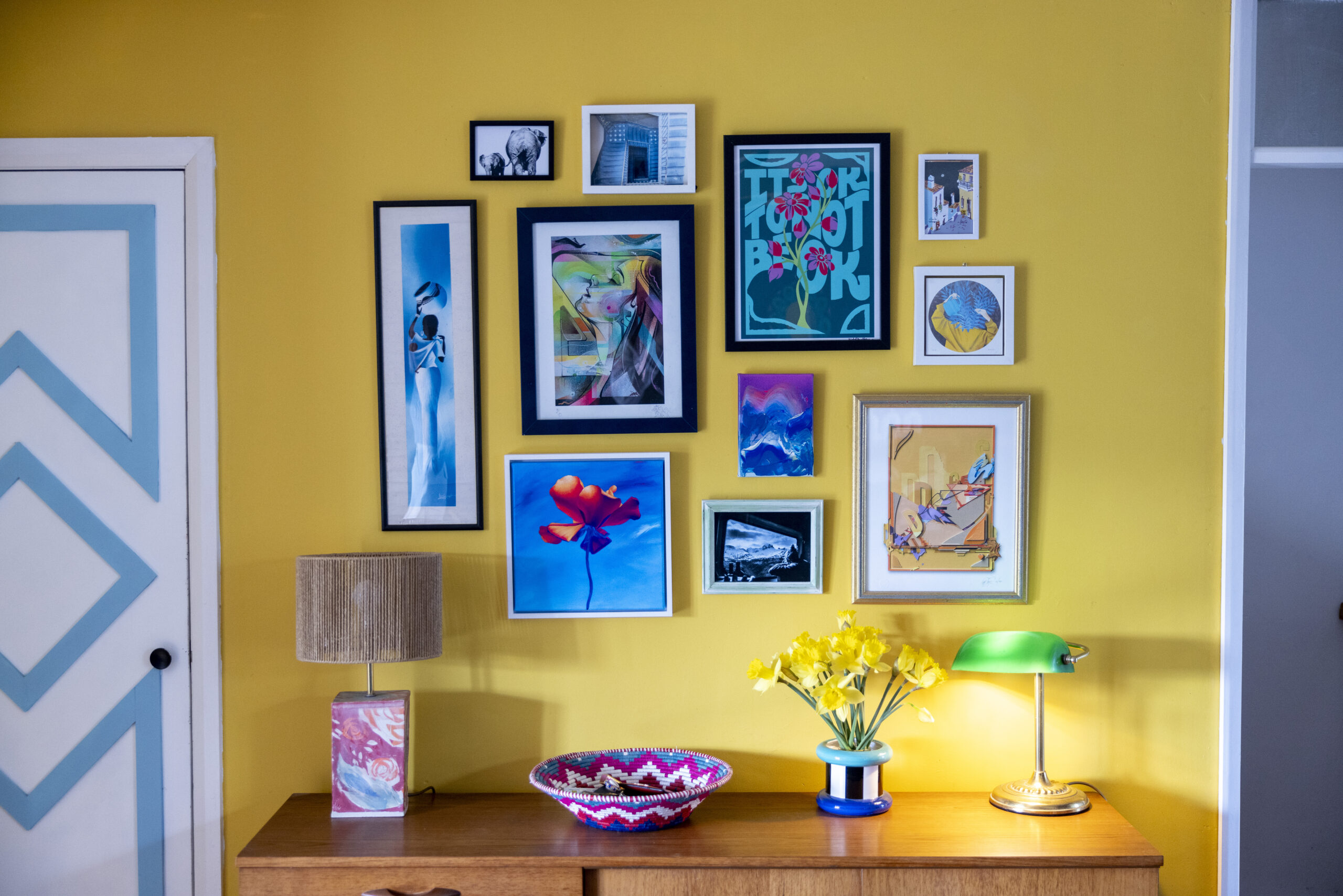 Artwork adorns a yellow wall above a dresser.
