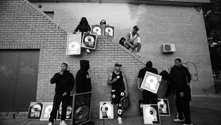 Black and white photograph showing the four core members of OneFour and six other young men, standing on and below a brick staircase, holding numerous framed records, with other framed records propped on the ground